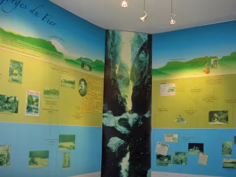 An exhibition room: a timeline of old photos and documents around a large photo of the torrent.