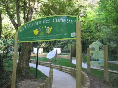 The entrance to the Clairière des Curieux: a wooden arch and a path lined with information panels.